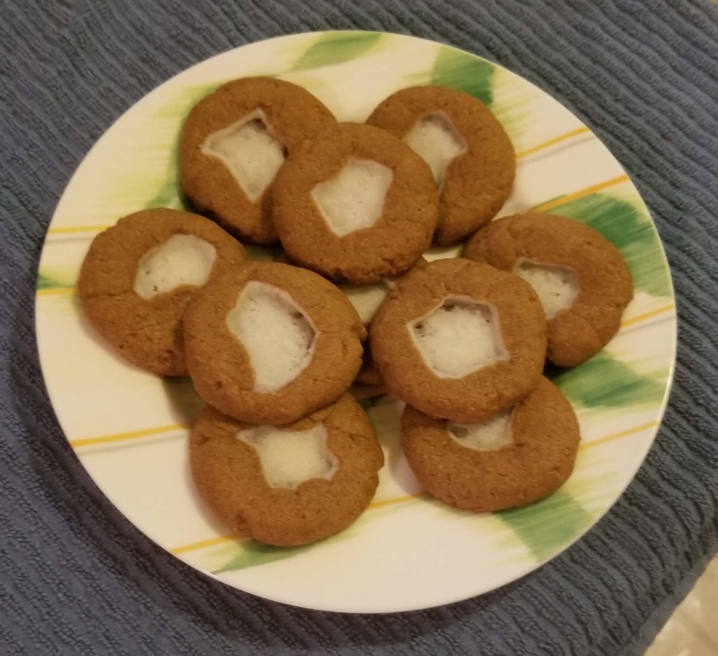 Photo of a plate of brown cookies with white cheese filling in the centers