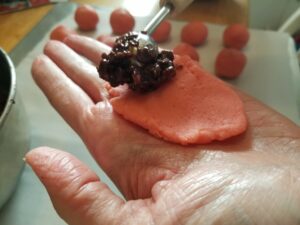 Hand holding a small flat piece of pink cookie dough, with a scoop of chocolate filling being placed on the dough.