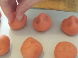 Balls of pink cookie dough, one at the far left being pinched in a three-finger grip and two to the right of it showing indentations from having already been pinched.