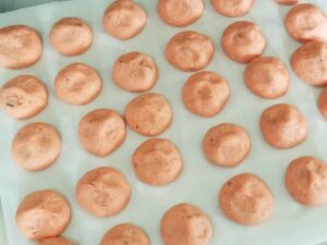 Baking sheet of finished pink cookies with three small indentations in the top of each.