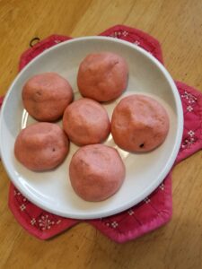 Six pink cookies with indented tops, on a small plate resting on a potholder.