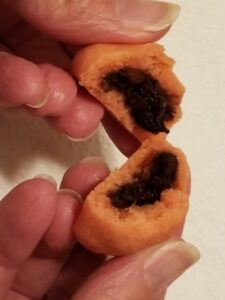 Two hands holding halves of a pink cookie with a chocolate center