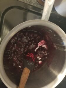 Metal saucepan containing cooked blueberry filling, with a pirate-printed rubber spatula showing the filling is thick enough to hold an edge when the bottom of the pot is scraped.