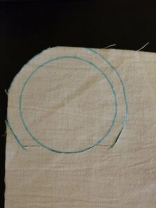 Off-white fabric with an inner circle traced in blue, an outer circle traced most of the way around, partly cut out.