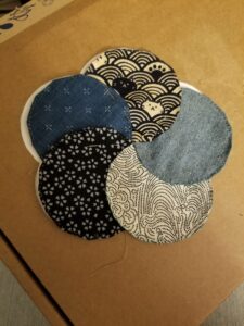 Five overlapping circles of patterned fabric, forming a flower shape. Patterns, clockwise from top: dark blue waves interspersed with cats and pawprints on an off-white background, plain light blue, wind/water swirls made of dark blue dots on off-white, five-petaled white flowers on navy blue, small white plus signs on medium dusty blue.